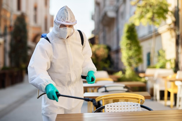 Healthcare worker in hazmat suit disinfecting sidewalk cafe during COVID19 epidemic