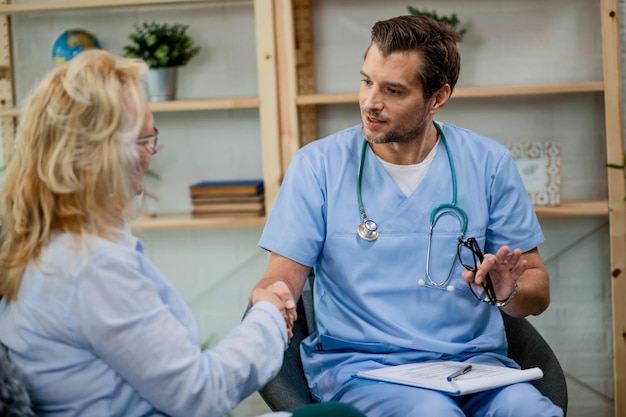 Healthcare worker shaking hands with female patient while being in a home visit