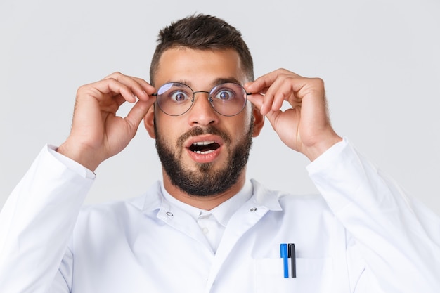 Healthcare workers, coronavirus, covid-19 pandemic and insurance concept. Close-up of excited and impressed hispanic doctor in white coat, put on glasses gasping and staring astonished.