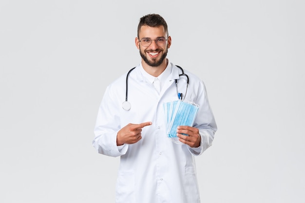 Free photo healthcare workers, medical insurance, pandemic and covid-19 concept. cheerful, smiling handsome doctor recommend using medical masks, physician in white scrubs and stethoscope ask stay safe.