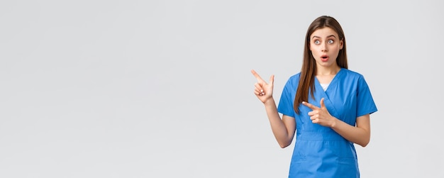 Free Photo healthcare workers prevent virus insurance and medicine concept surprised female nurse or doctor in blue scrubs looking and pointing fingers upper left corner gasping amazed