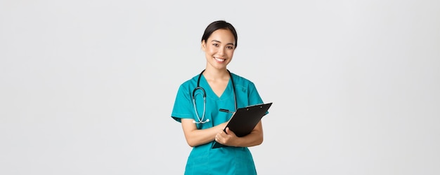 Free Photo healthcare workers, preventing virus, quarantine campaign concept. cheerful friendly asian female physician, doctor with clipboard during daily checkup, standing white background.