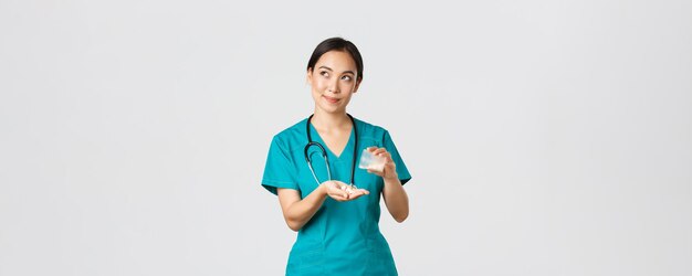 Healthcare workers, preventing virus, quarantine campaign concept. Thoughtful and caring smiling asian female nurse, intern in scrubs handle medication to patient and looking dreamy upper left corner.