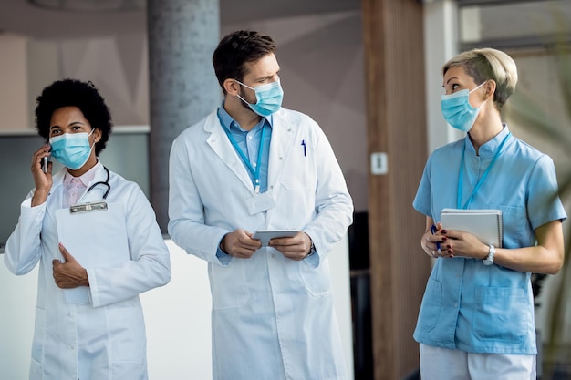 Free photo healthcare workers with face masks talking while walking through a hallway at the hospital