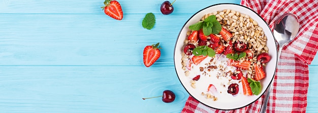 Healthy breakfast - granola, strawberries, cherry, nuts and yogurt in a bowl on a wooden table. Vegetarian concept food. Top view