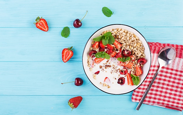 Healthy breakfast - granola, strawberries, cherry, nuts and yogurt in a bowl on a wooden table. Vegetarian concept food. Top view