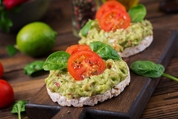 Healthy breakfast. Sandwich crisp bread with guacamole and tomatoes on a wooden table.