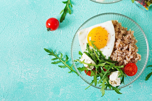 Healthy breakfast with egg, feta cheese, arugula, tomatoes  and buckwheat porridge on light background. Proper nutrition. Dietary menu. Flat lay. Top view