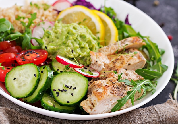 Healthy dinner. Buddha bowl lunch with grilled chicken and quinoa, tomato, guacamole, red cabbage, cucumber and arugula.