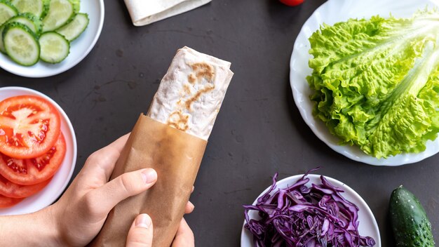 Healthy food composition. Vegetables on dishes and male hands holding a pita roll