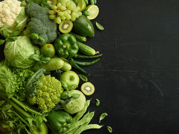 Healthy food dish on black stone background. Healthful set including vegetables and fruits. Grape, apple, kiwi, pepper, lime, cabbage, zucchini, grapefruit. Proper nutrition or vegetarian menu.