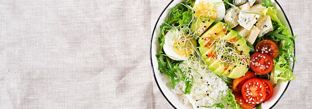 Free photo healthy green vegetarian buddha bowl lunch with eggs, rice, tomato, avocado and blue cheese on table.