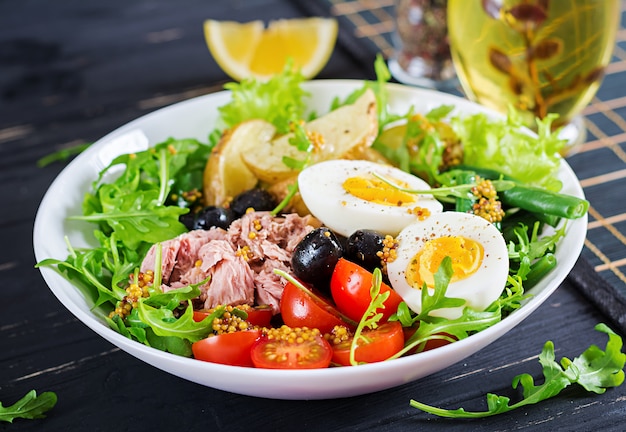 Free photo healthy hearty salad of tuna, green beans, tomatoes, eggs, potatoes, black olives close-up in a bowl on the table.