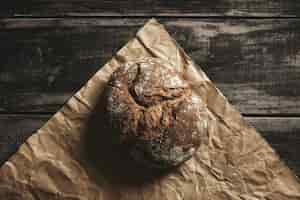 Free photo healthy rye whole grain round bread on brown craft paper isolated on black farm woden table. home baked.