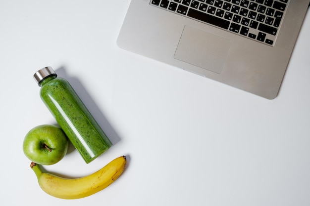 Healthy working life style Laptop with stationery and green smoothies with apple on white table Top view flat lay