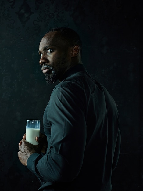 Healthy young african man holding cup of milk on a black studio background.