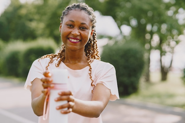 Healthy young african woman outdoors in morning. Girl with bottle of water.