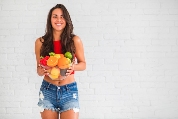 Healthy young woman holding fresh vegetables and fruits in bowl