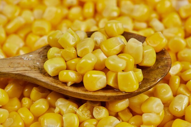 A heap of boiled sweet corn with a wooden spoon on a white table.