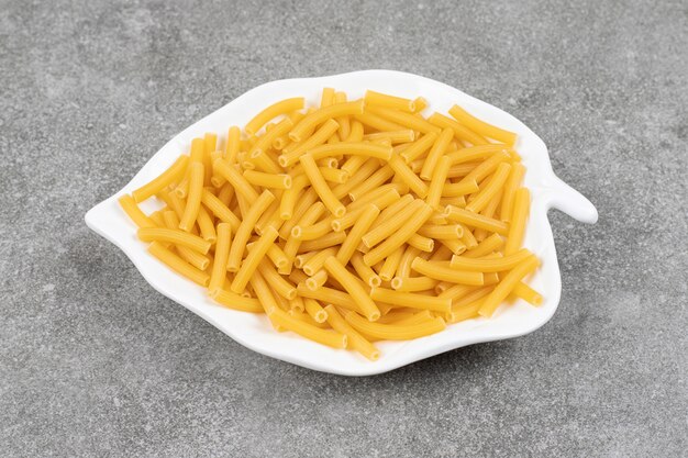 Heap of raw macaroni on white plate