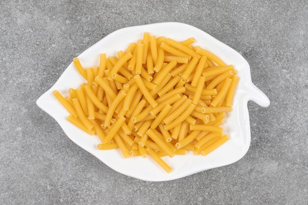 Heap of raw macaroni on white plate