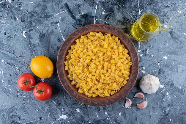 Free Photo heap of raw pipette rigate pasta in a bowl with fresh red tomatoes and oil.