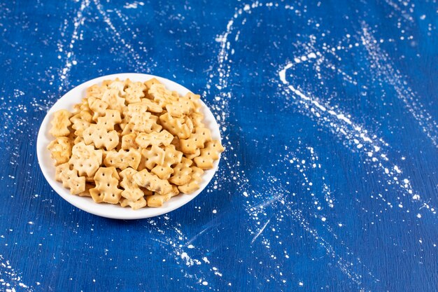 Heap of salty small crackers placed on white plate.