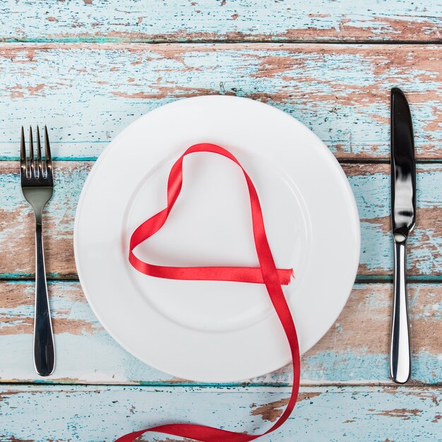 Heart shape from red ribbon on plate with cutlery