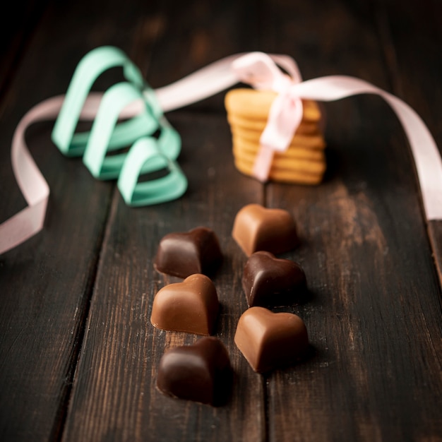 Free photo heart-shaped chocolates with cookies and ribbon