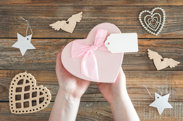 Free photo heart shaped gift box with blank gift tag in female hands on wooden background