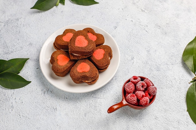 Heart shaped valentine cookies with frozen raspberries on light background