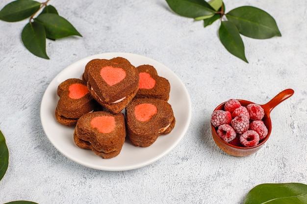 Heart shaped valentine cookies with frozen raspberries on light background