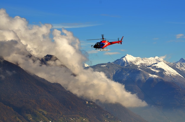 Helicopter flying among the clouds above the snow-capped mountains