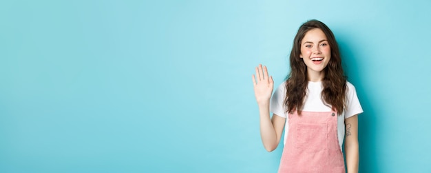 Free Photo hello nice to meet you beautiful friendly girl waving hand to say hi looking happy and smiling while