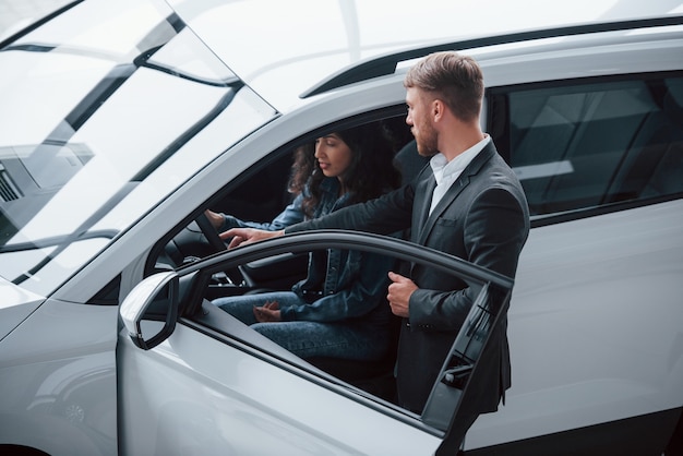 Helping girl to decide. Female customer and modern stylish bearded businessman in the automobile saloon