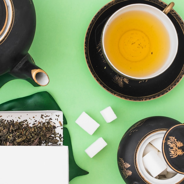 Herbal tea cup with sugar cubes on green background