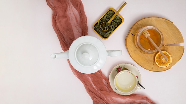 Free photo herbal teapot; leaves; honey dipper; dried citrus; ceramic cup and saucer on white background