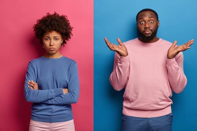 Free photo hesitant black man spreads palms with hesitation, doesnt know how to calm girlfriend who stands offended with arms folded