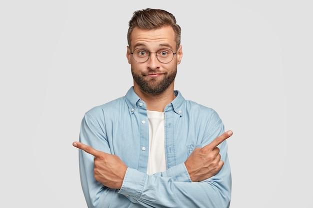 Free photo hesitant and clueless man crosses hands over chest, indicates with index fingers in different sides or directions