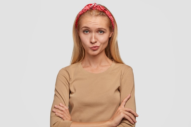 Free photo hesitant light haired girl purses lips, keeps hands crossed, feels clueless