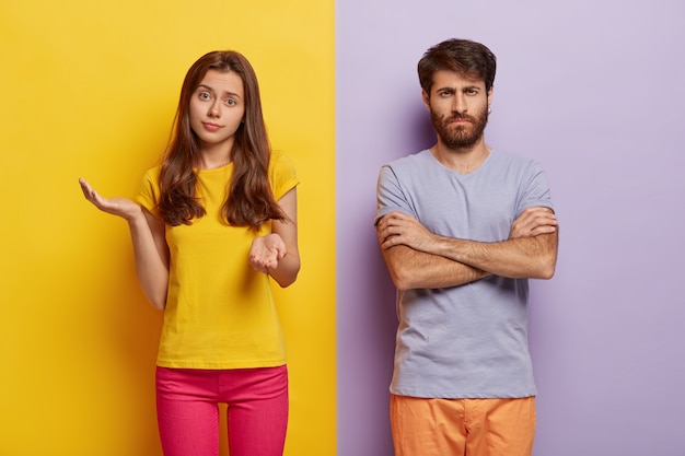 Free photo hesitant young woman spreads hands with doubt, wears casual clothes, dissatisfied man keeps hands crossed, discontent with something