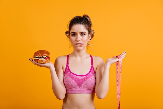 Free photo hesitating woman holding cheeseburger