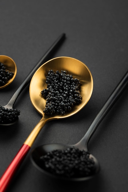 High angle of black and golden spoons with caviar