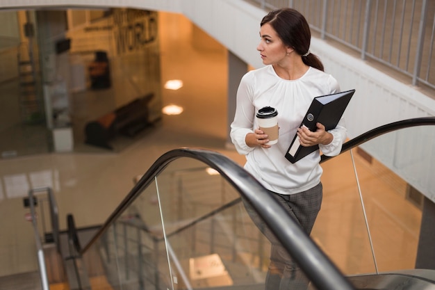 Free photo high angle of businesswoman with binder and coffee on escalator