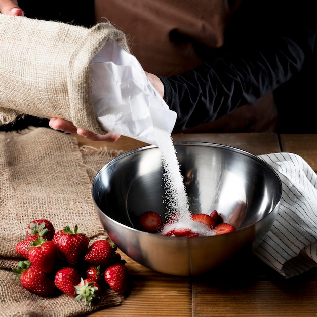 High angle of chef adding sugar to bowl of strawberries