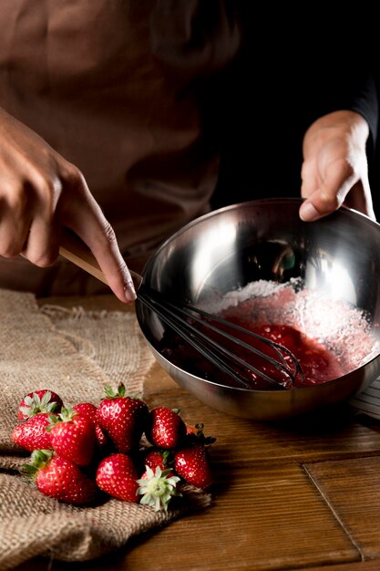 High angle of chef whisking strawberries in bowl with sugar