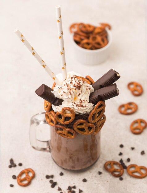 High angle of chocolate milkshake glass with pretzels and straws