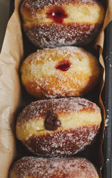 High angle closeup of fluffy doughnuts filled with jam in a container under the lights