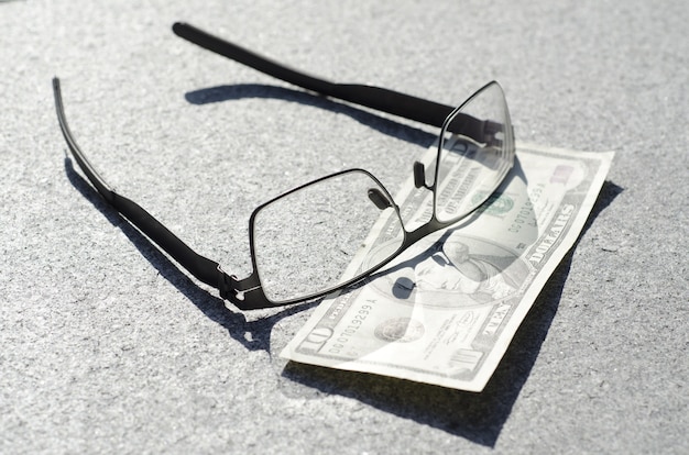 Free Photo high angle closeup shot of eyeglasses on a ten-dollar on a grey surface