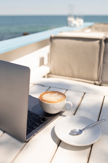 Free Photo high angle coffee cup and laptop at seaside